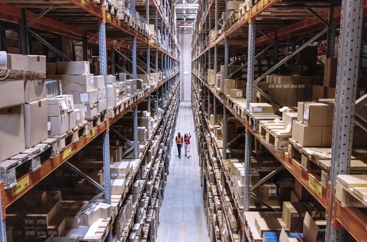 High angle view of a warehouse manager walking with foremen checking stock on racks.