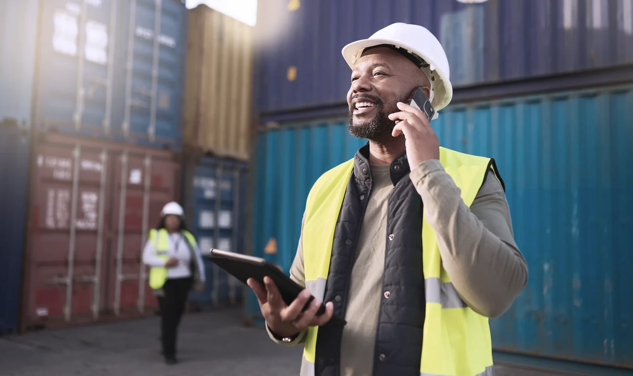 Logistics, shipping and construction worker on the phone with tablet in shipyard.