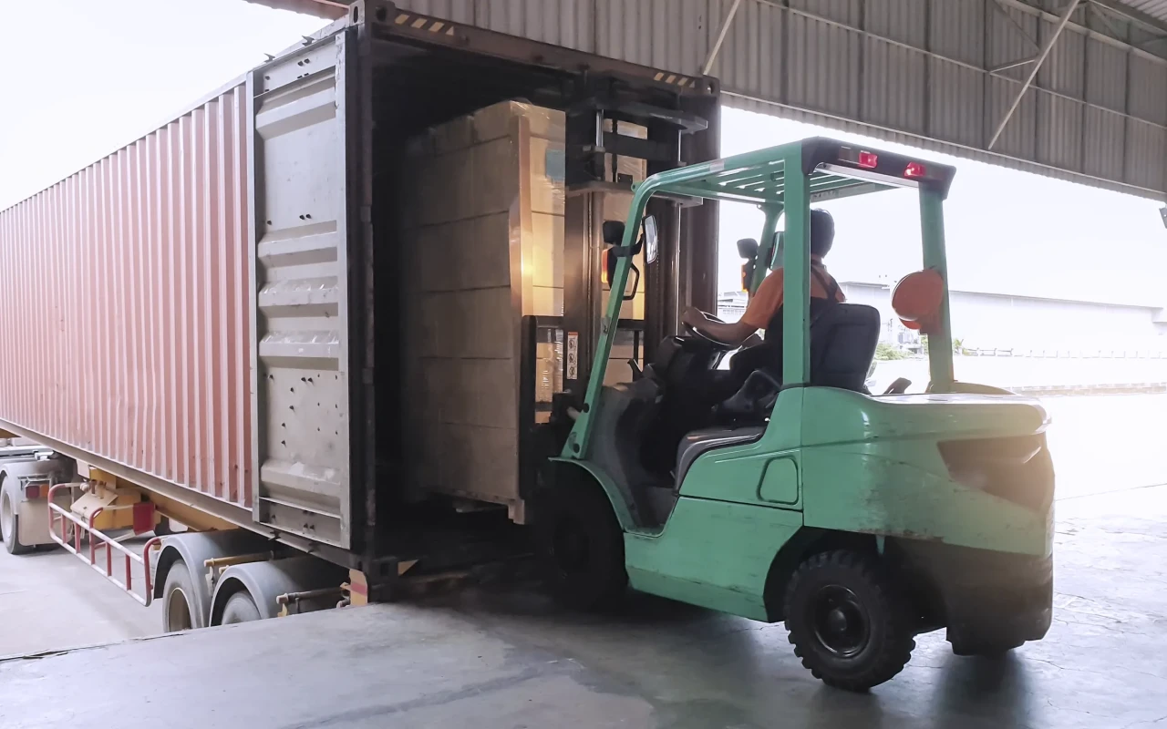 Forklift driver loading goods pallet into the truck containe.