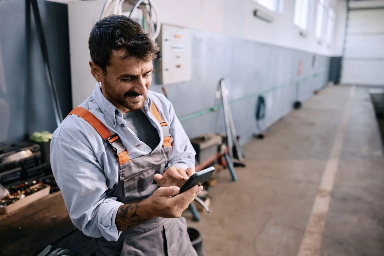 Happy mechanic using smart phone while working in a repair shop.